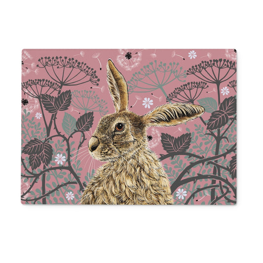 This rectangular worktop saver design features a hare portrait with one floppy ear, around the hare are stylised brambles, leaves, cow parsley and dandelion puffs, background colour is an antique rose pink.