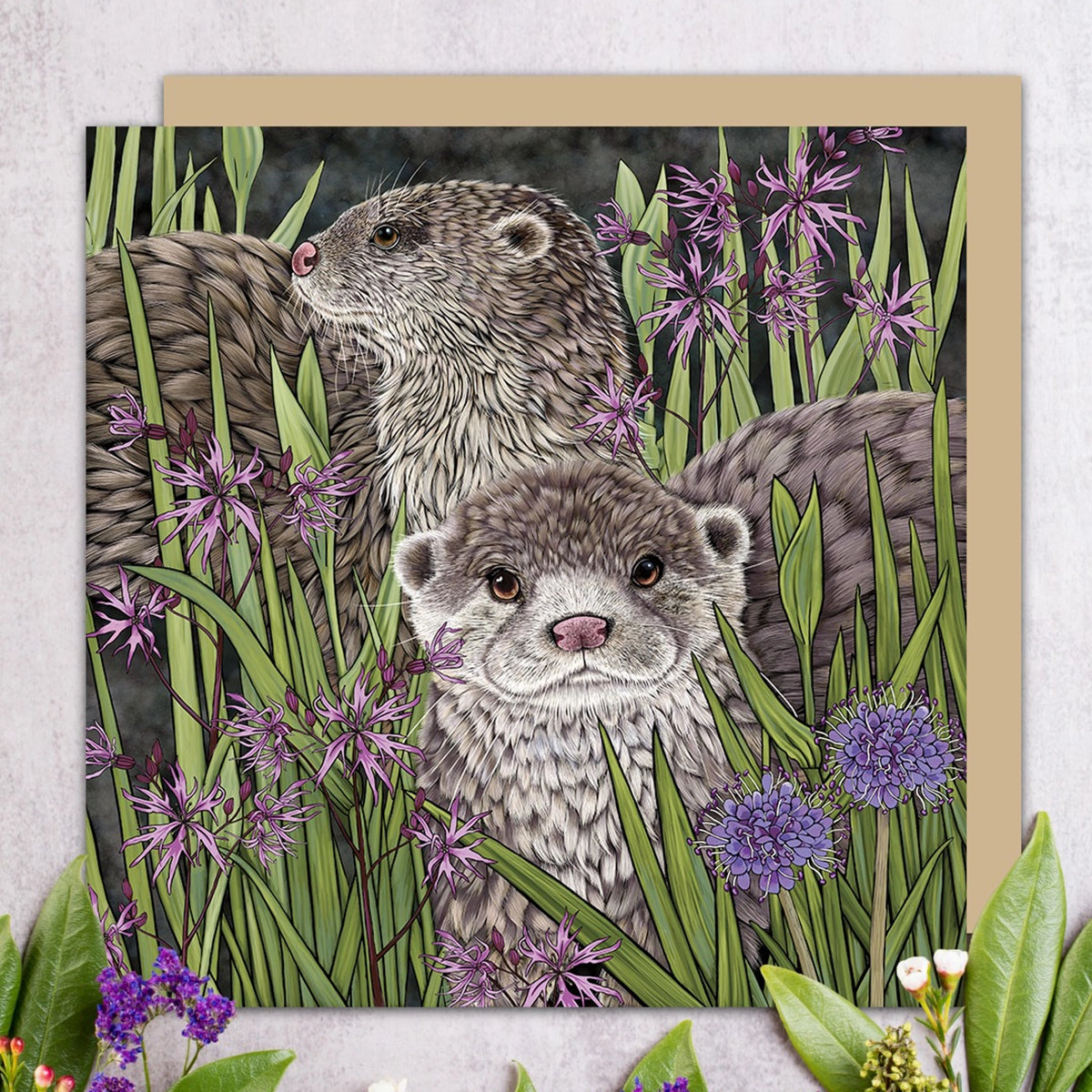 A square art card featuring an illustrated pair of otters among green reeds and purple flowers, displayed against a dark textured background with decorative greenery at the bottom.