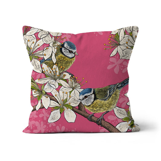 This illustrated blue tits square cushion features two cute blue tits perched in a hedgerow of hawthorn blossom, background is a contrasting deep pink.